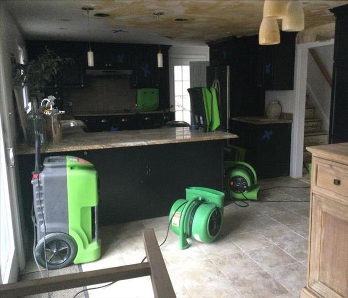 Air movers and dehumidifiers operating in a kitchen with heavily water-damaged walls and ceiling