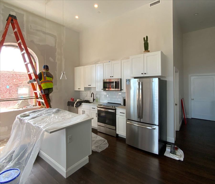 SERVPRO tech on ladder in kitchen with plastic on island