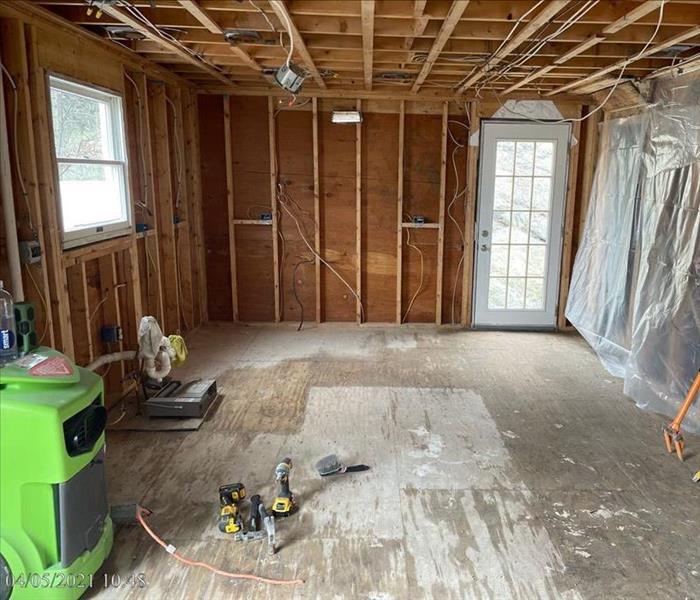 SERVPRO dehumidifier and tools in a partially sealed room with removed drywall, insulation, and flooring