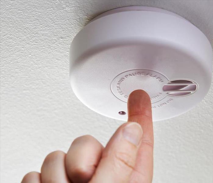 A finger pushing a button on a smoke detector